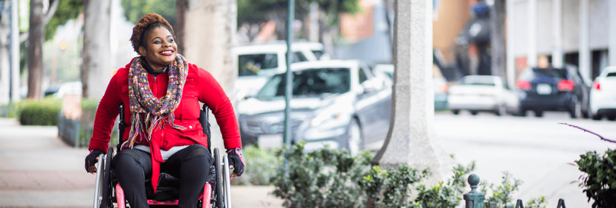 woman in wheelchair traveling along sidewalk
